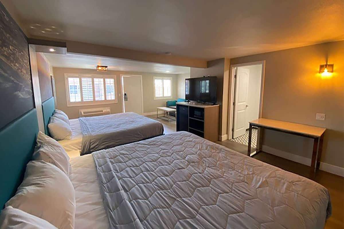A hotel room with two beds, a television, a desk, and a bench.