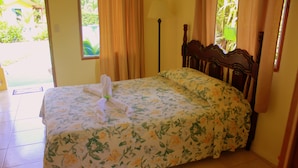 Una cama bien hecha con ropa de cama floral, un cabecero de madera y una ventana con cortinas.