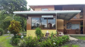 Zona de recepción con un cartel, un pequeño jardín y un edificio al fondo.