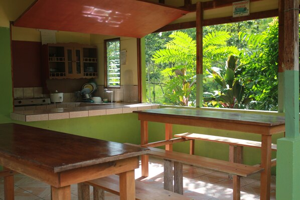 A kitchen with a wooden table and bench, a window with a view of greenery, and a sign above the window.