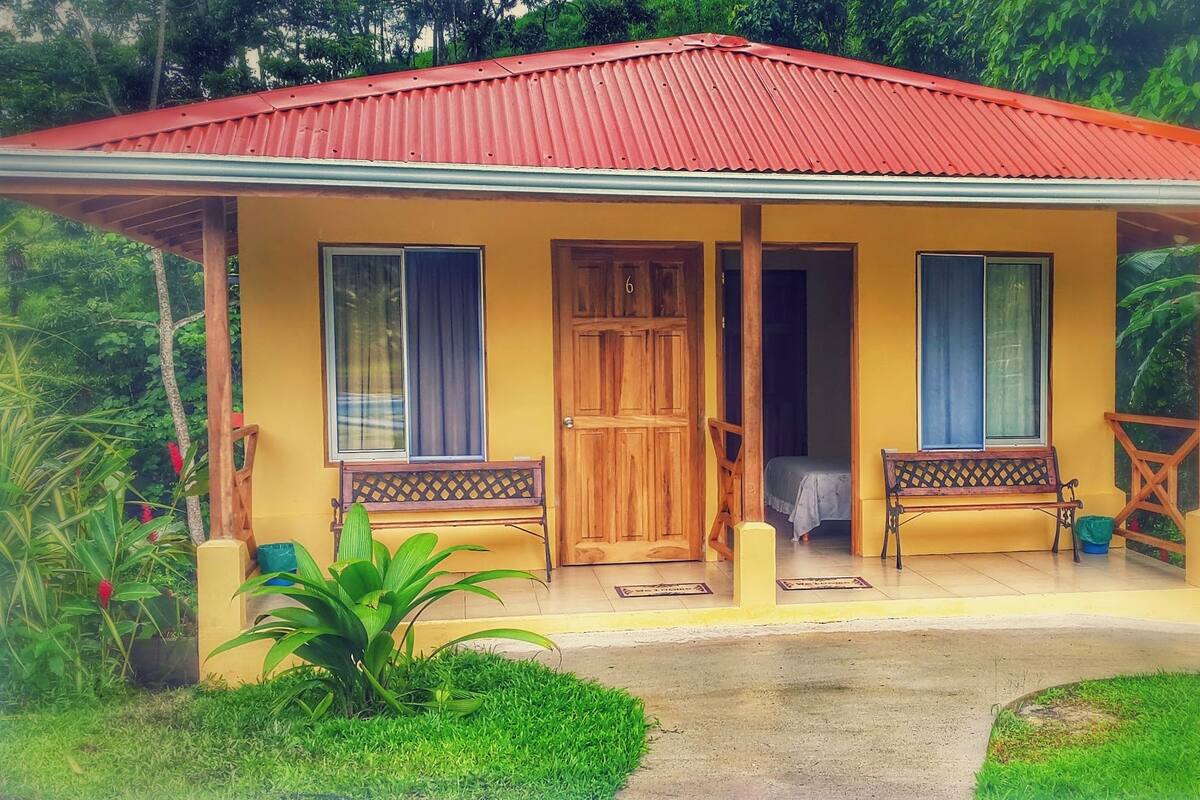 Un bâtiment jaune avec un toit rouge, des portes en bois et des bancs à l’extérieur.