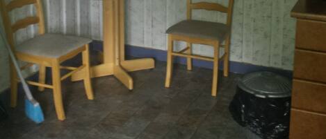 A small dining area with two wooden chairs and a round table, a broom, and a trash can.