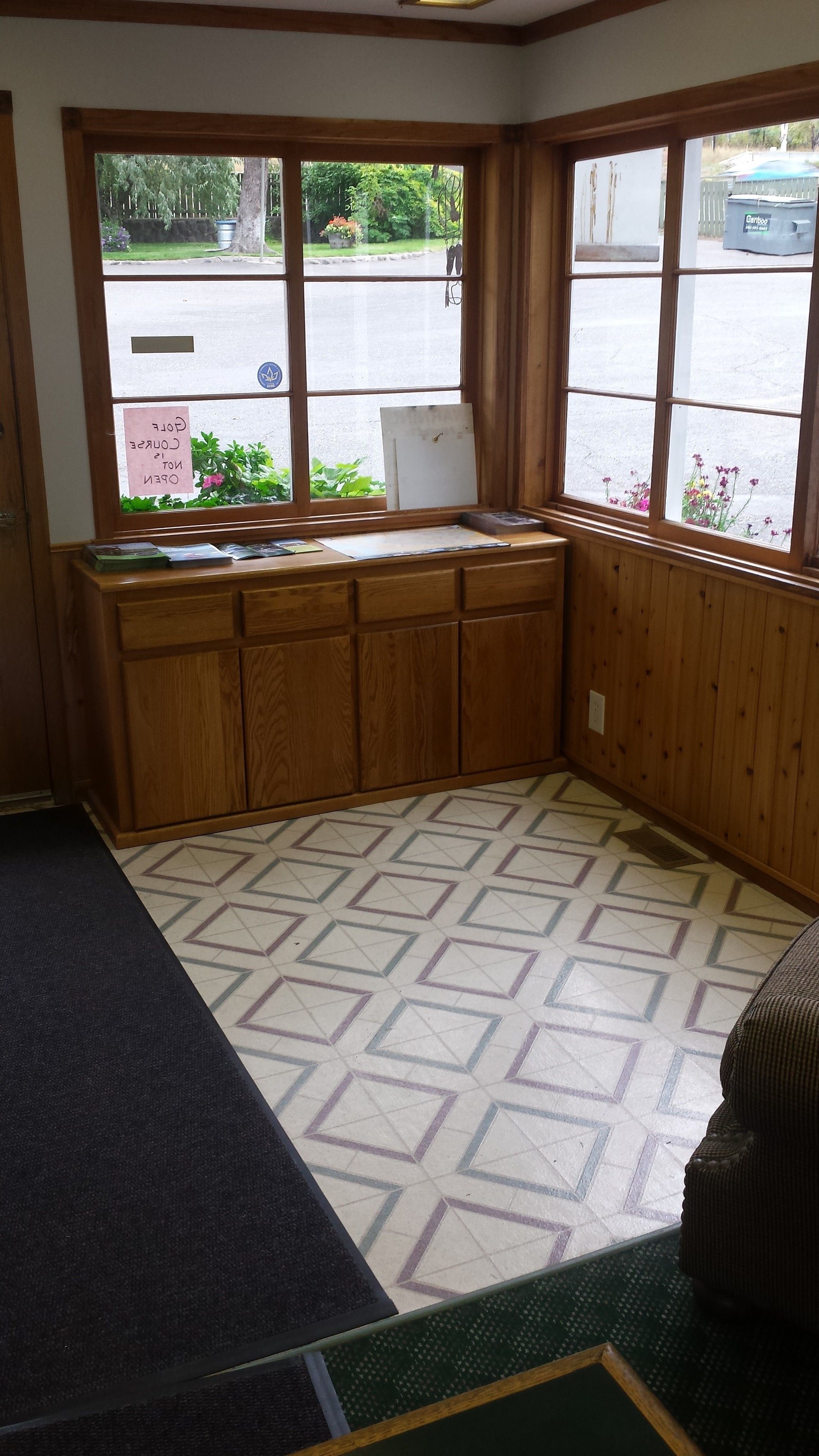A corner room with a wooden bench, a window with a view of the street, and a patterned floor.