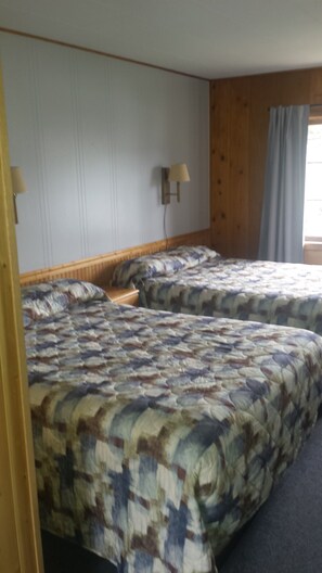 A room with two beds, a wooden headboard, a wall-mounted lamp, and a window with curtains. - Lakeside Motel (Williams Lake)