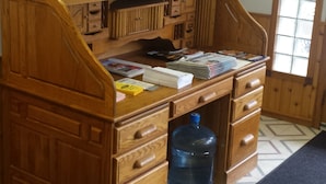 Escritorio de madera con cajones, un reloj y varios objetos encima, como libros y un dispensador de agua.