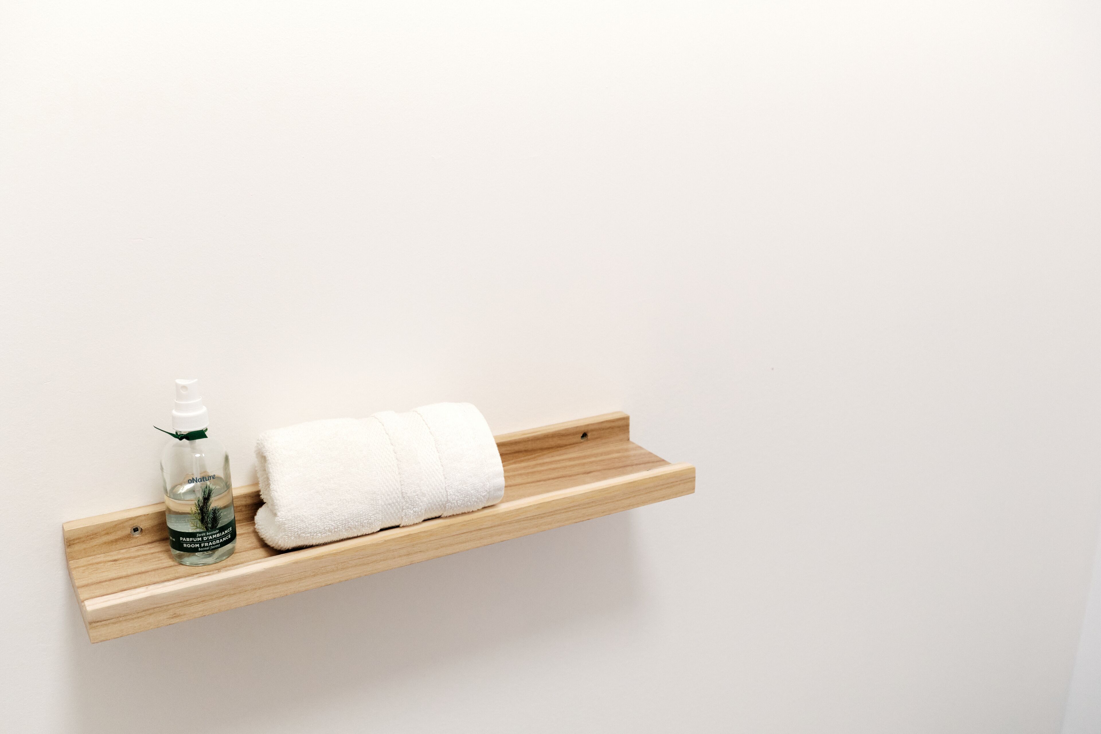 A wooden shelf with a bottle of lotion and a rolled white towel.