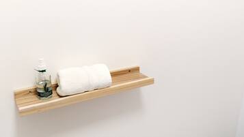 A wooden shelf with a bottle of lotion and a rolled white towel.