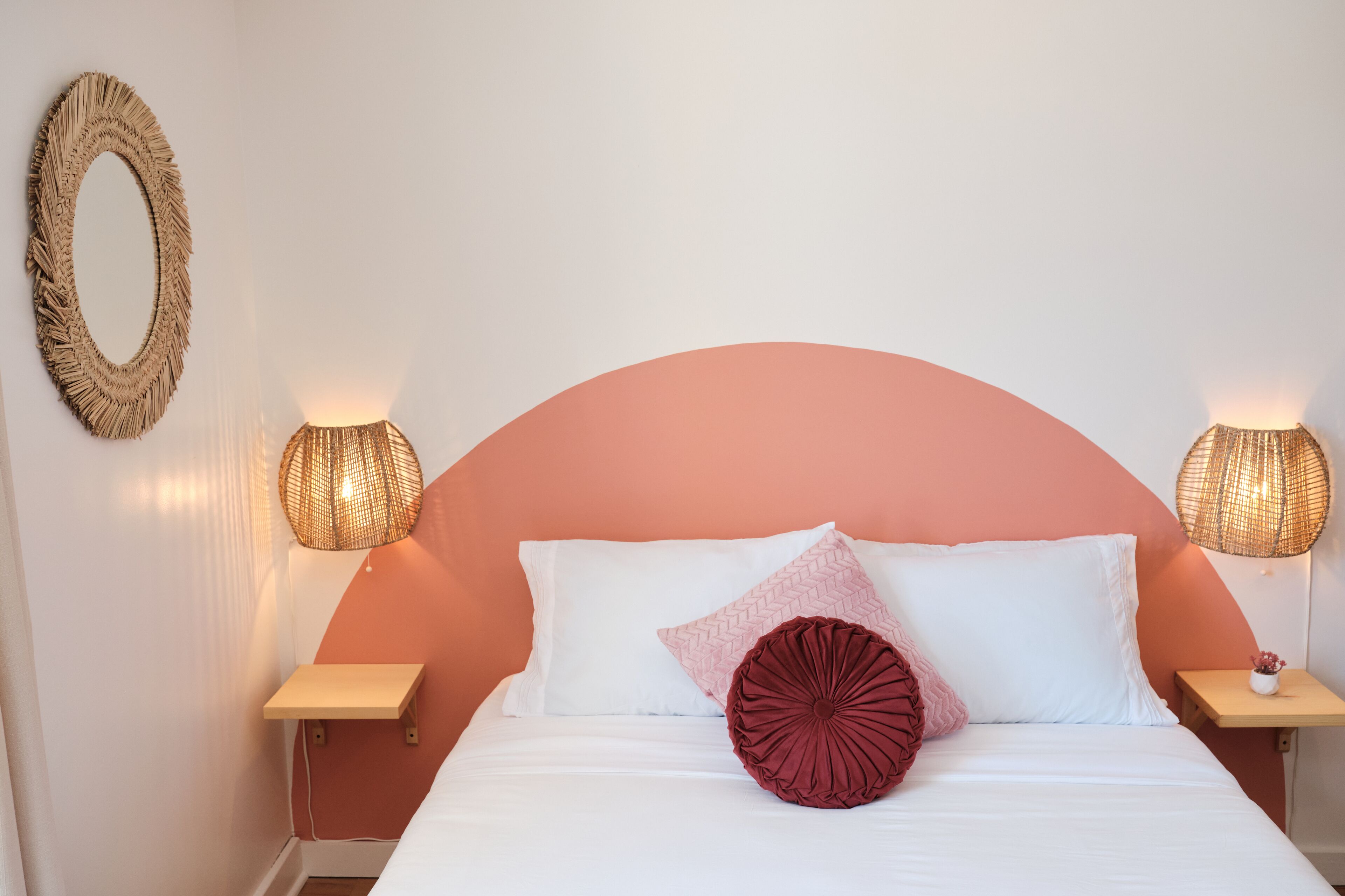 A bedroom with a curved headboard, two bedside lamps, a mirror, and a bedside table with a small plant.