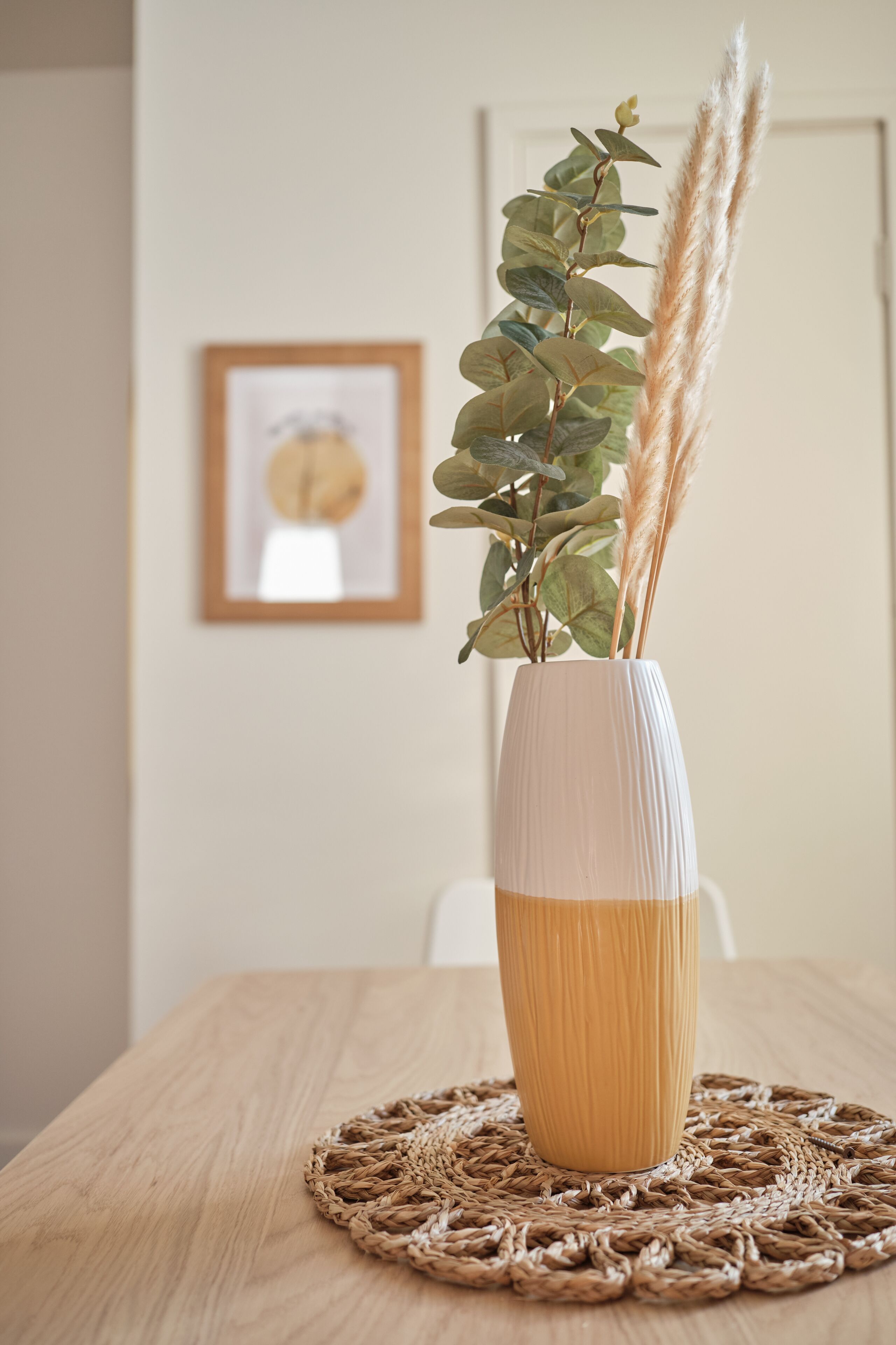 A white vase with a textured pattern on a wooden table, placed on a woven placemat.