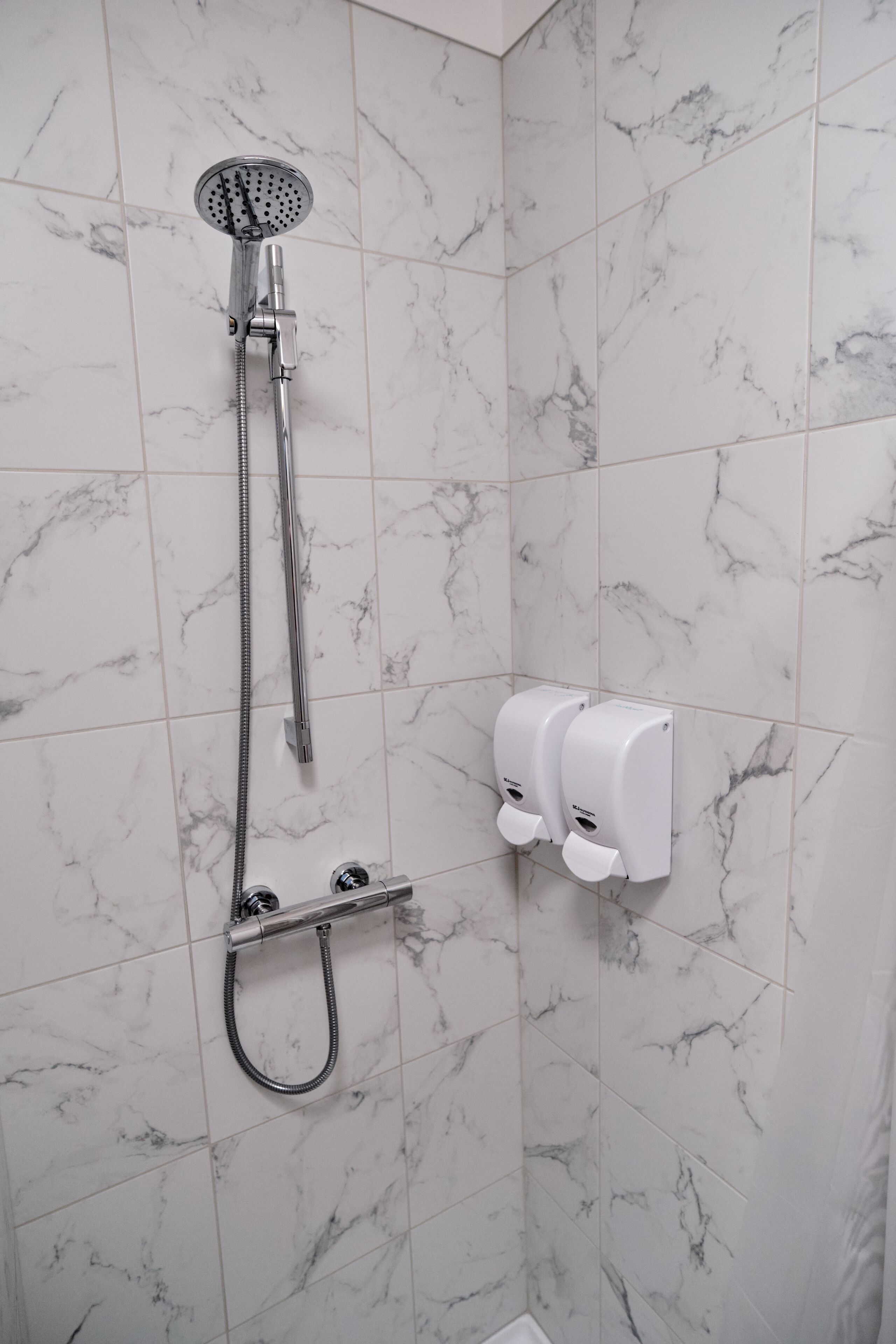 A shower with a handheld showerhead, a handheld shower attachment, and a wall-mounted soap dispenser.