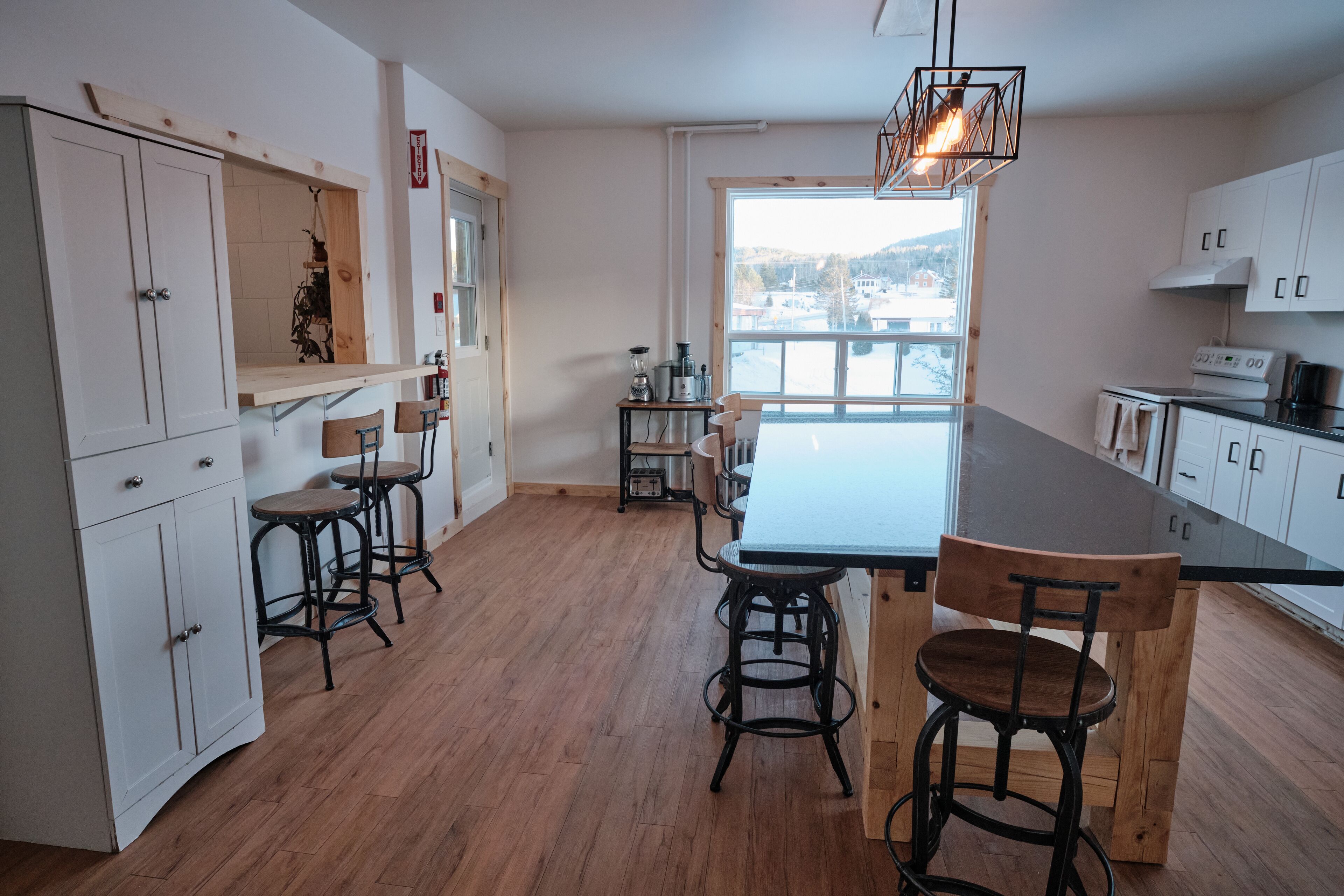 A modern kitchen with wooden flooring, white cabinets, and a large window offering a view of the outside.