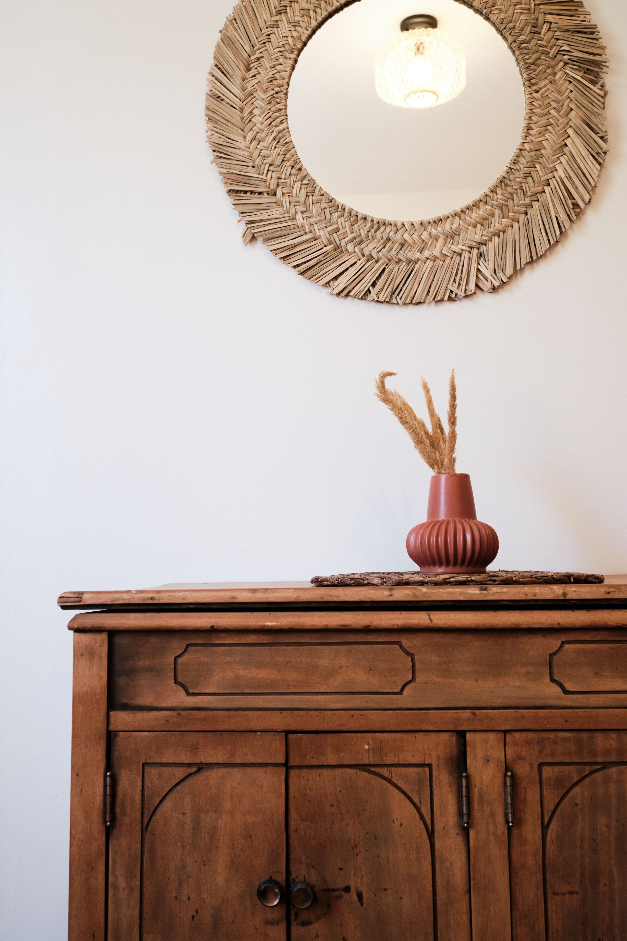 Un mueble de madera con un espejo encima y un florero con plantas secas sobre su superficie.