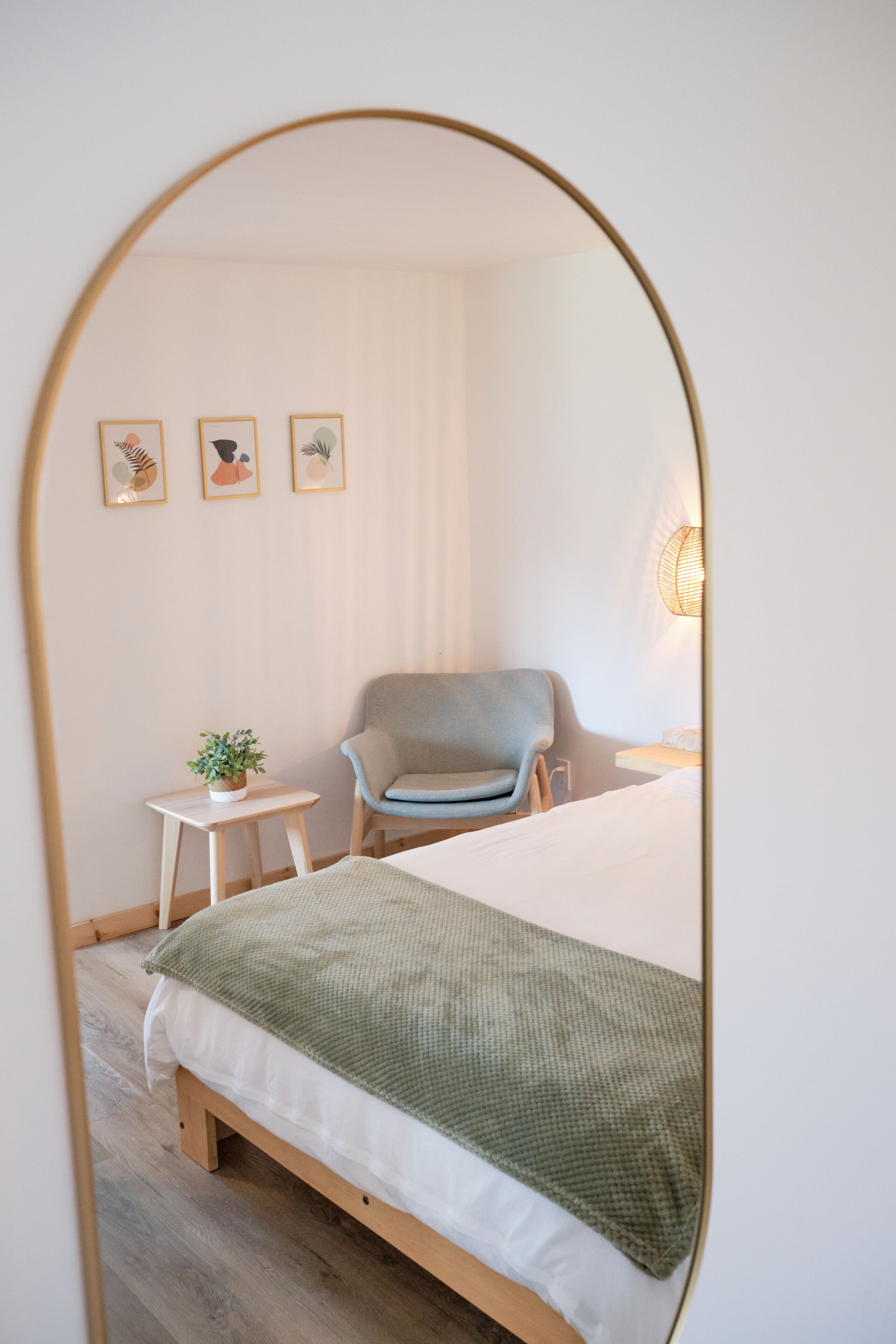Une chambre à coucher avec un lit, une chaise, une petite table sur laquelle se trouve une plante, et trois tableaux encadrés accrochés au mur.