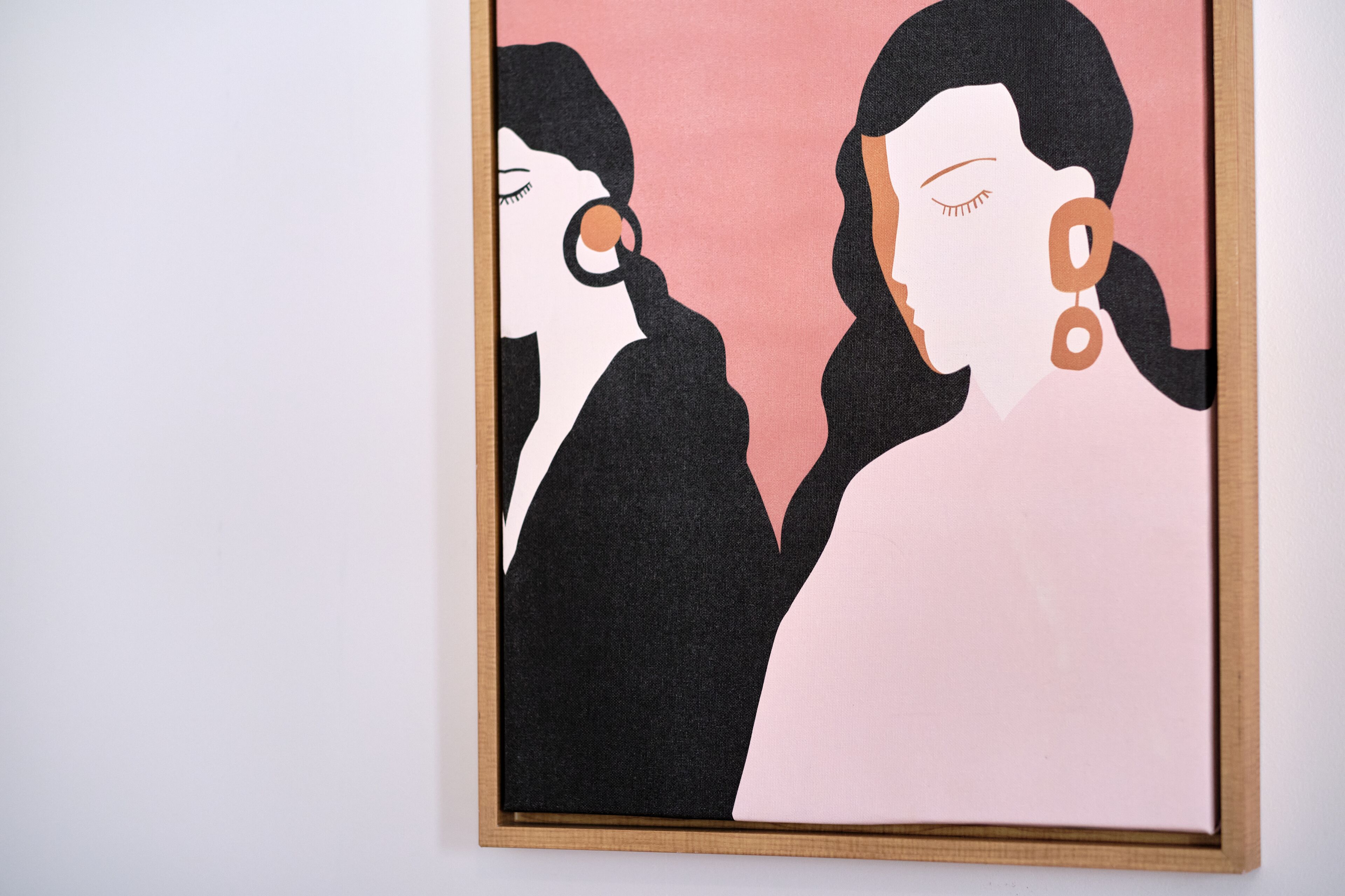A framed artwork with two stylized figures against a pink background.