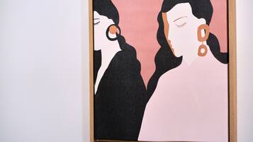 A framed artwork with two stylized figures against a pink background.