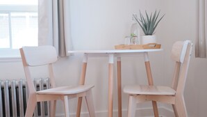 Una habitación con una mesa blanca y dos sillas de madera, un radiador y una ventana con cortinas.