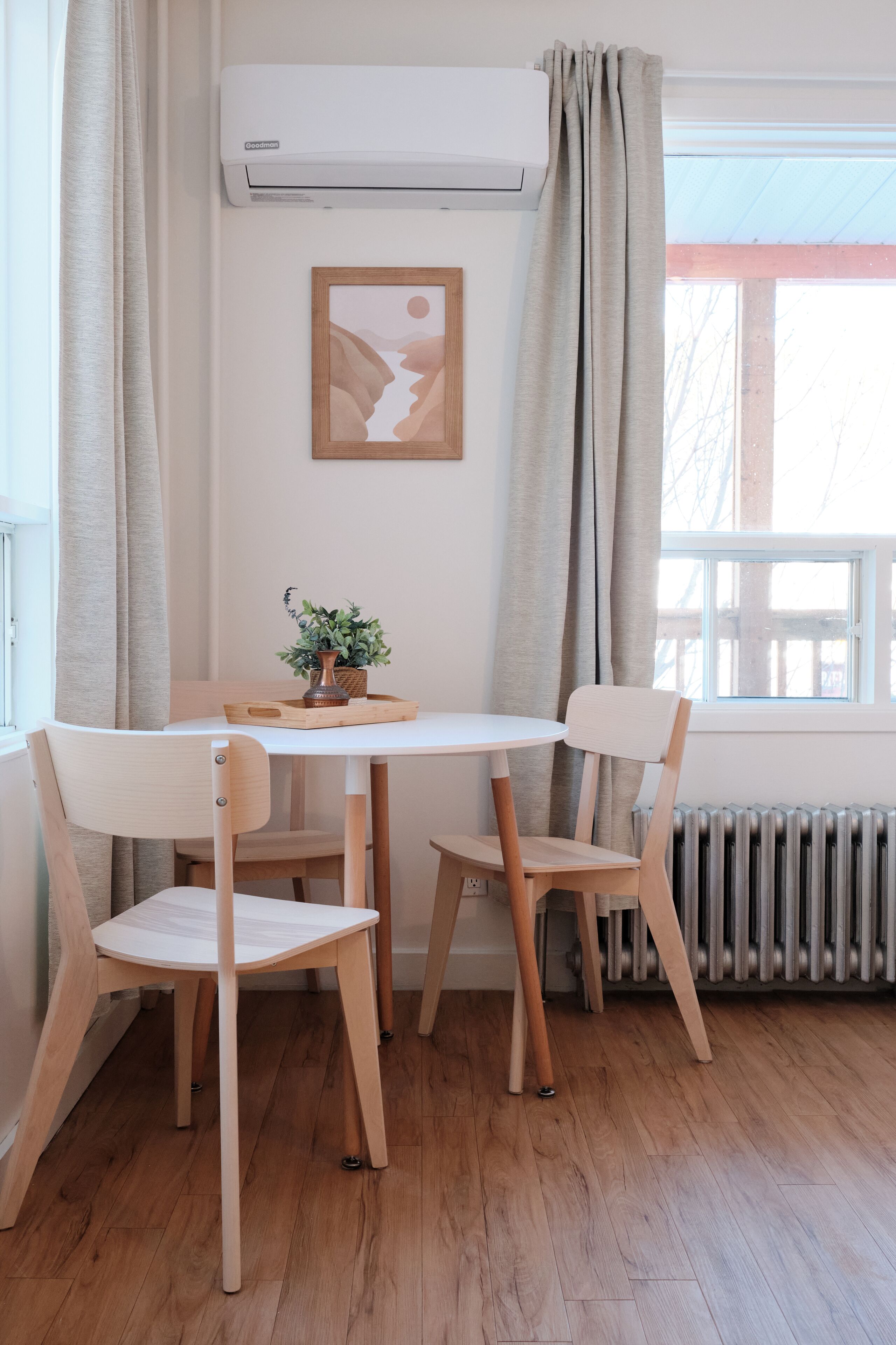 A dining area with a round table, two chairs, a vase with plants, and a framed picture on the wall.