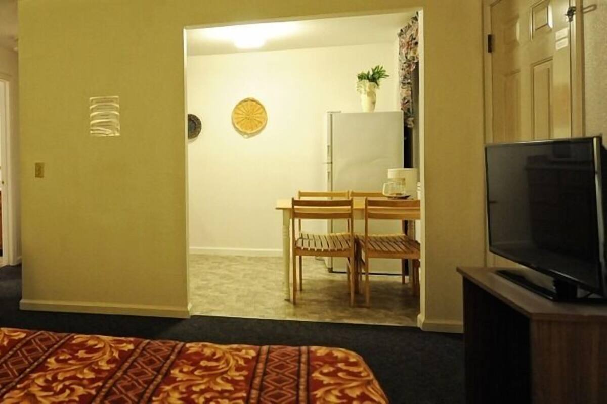 A hotel room with a bed, a TV, a desk with chairs, and a door leading to a bathroom.