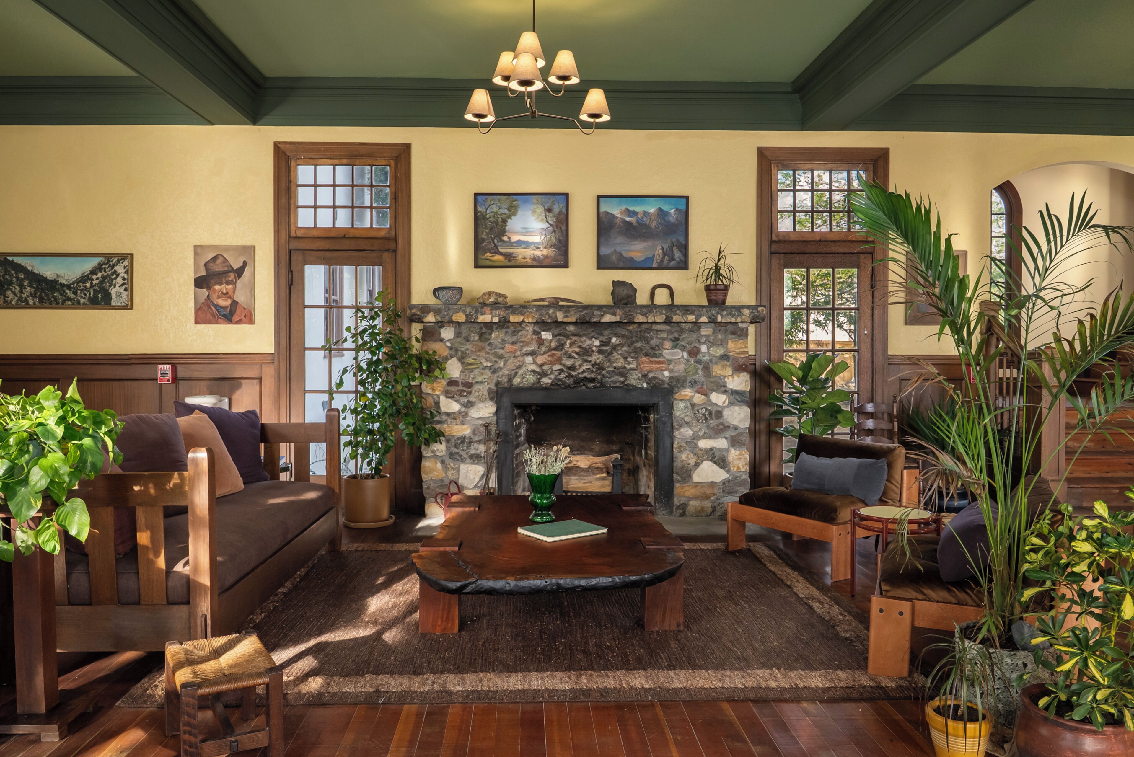 A cozy living room with a stone fireplace, wooden furniture, and various plants.