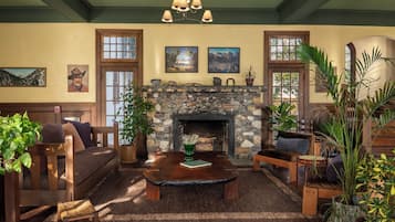 A cozy living room with a stone fireplace, wooden furniture, and various plants.