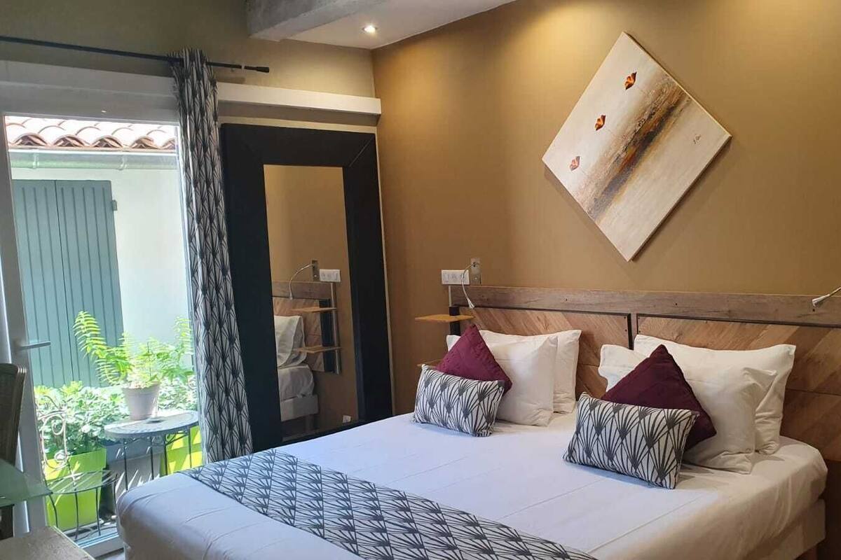 A hotel room with a bed, a headboard, a wall-mounted artwork, and a view of a balcony with plants.
