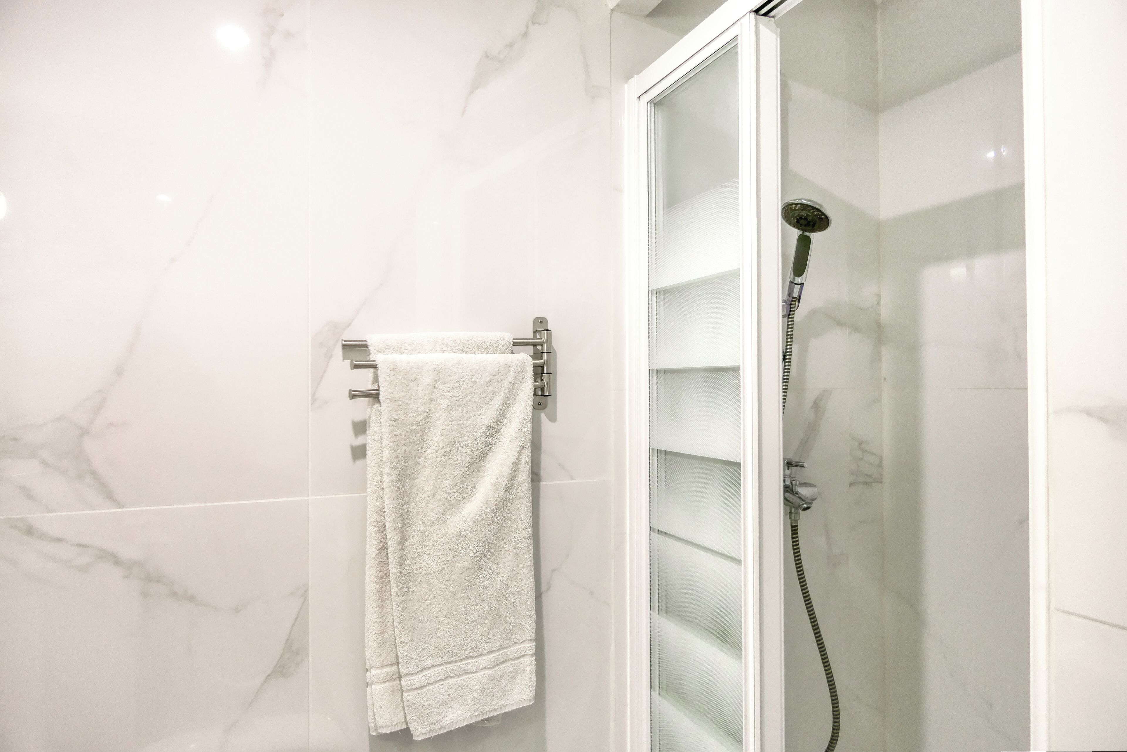 Un baño con cabina de ducha de vidrio, un perchero con toalla y paredes de mármol.