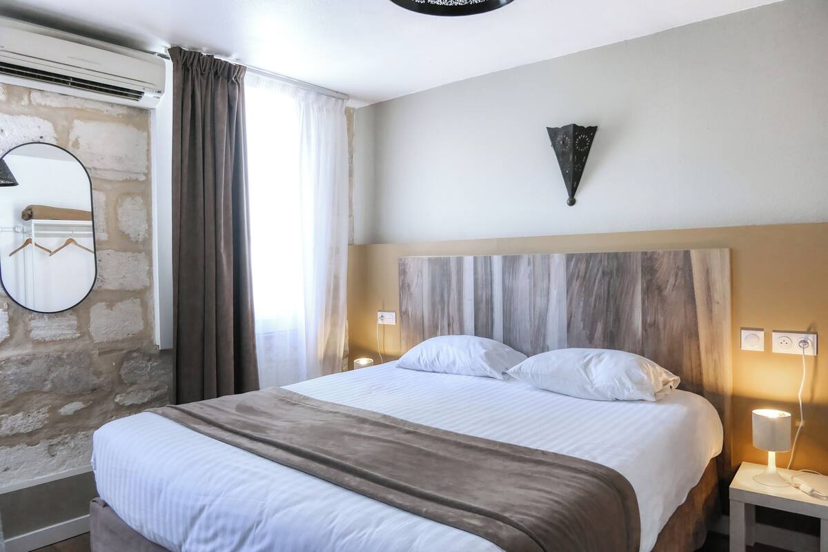 A hotel room with a large bed, a stone wall, a mirror, a nightstand, and a wall-mounted light fixture.