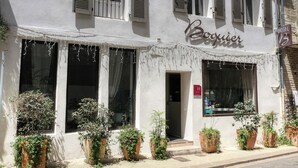 Un bâtiment sur lequel on peut lire l’inscription « Boquier », et au-dessus de l’entrée, une enseigne indiquant « HÔTEL ». Des plantes en pot sont disposées devant l’entrée.
