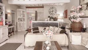 Un salon bien éclairé, avec un canapé, une table basse, une horloge et un vase rempli de fleurs.