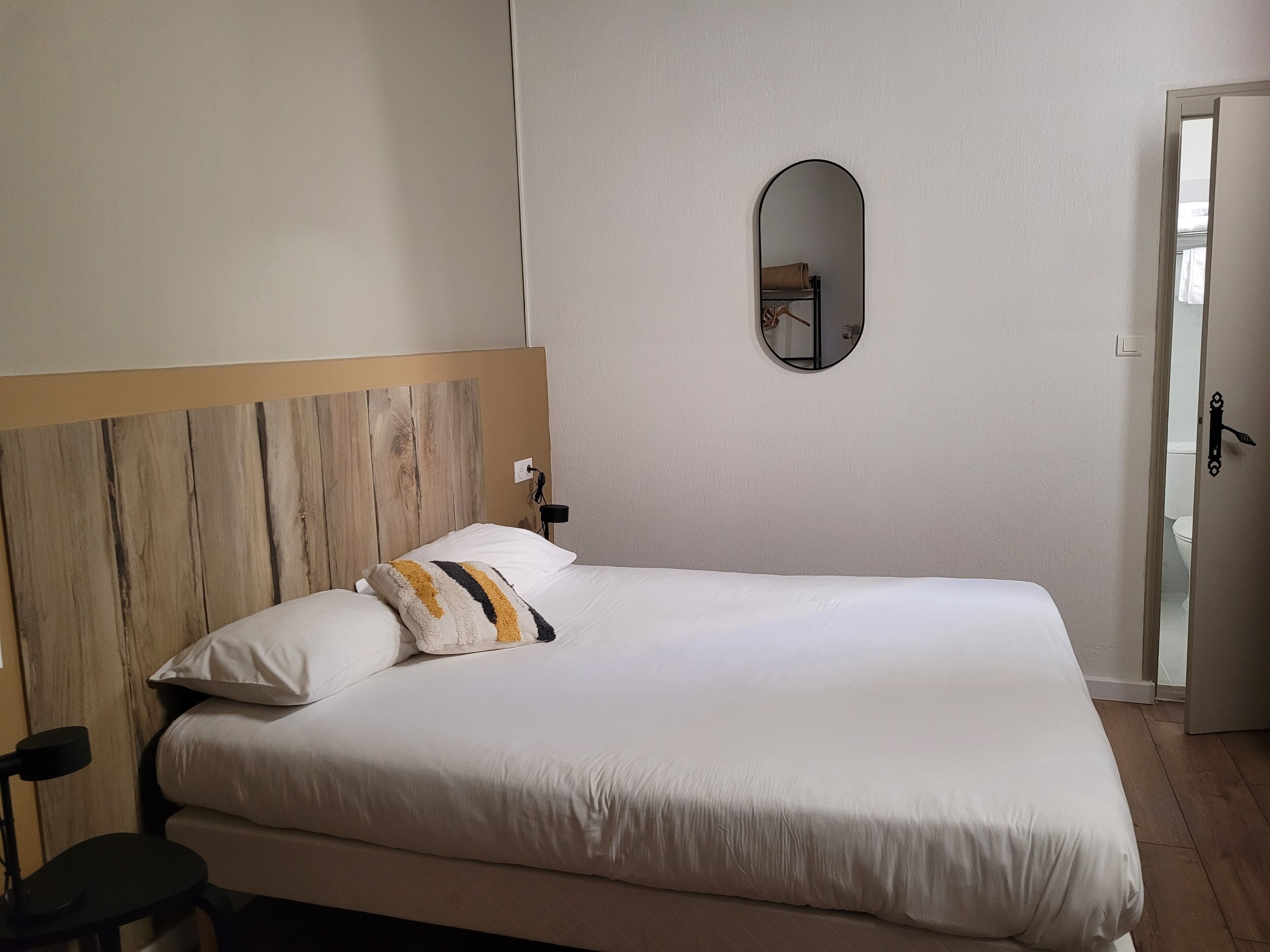 Una cama bien hecha con cabecera de madera, una mesita de noche y un espejo redondo en la pared.