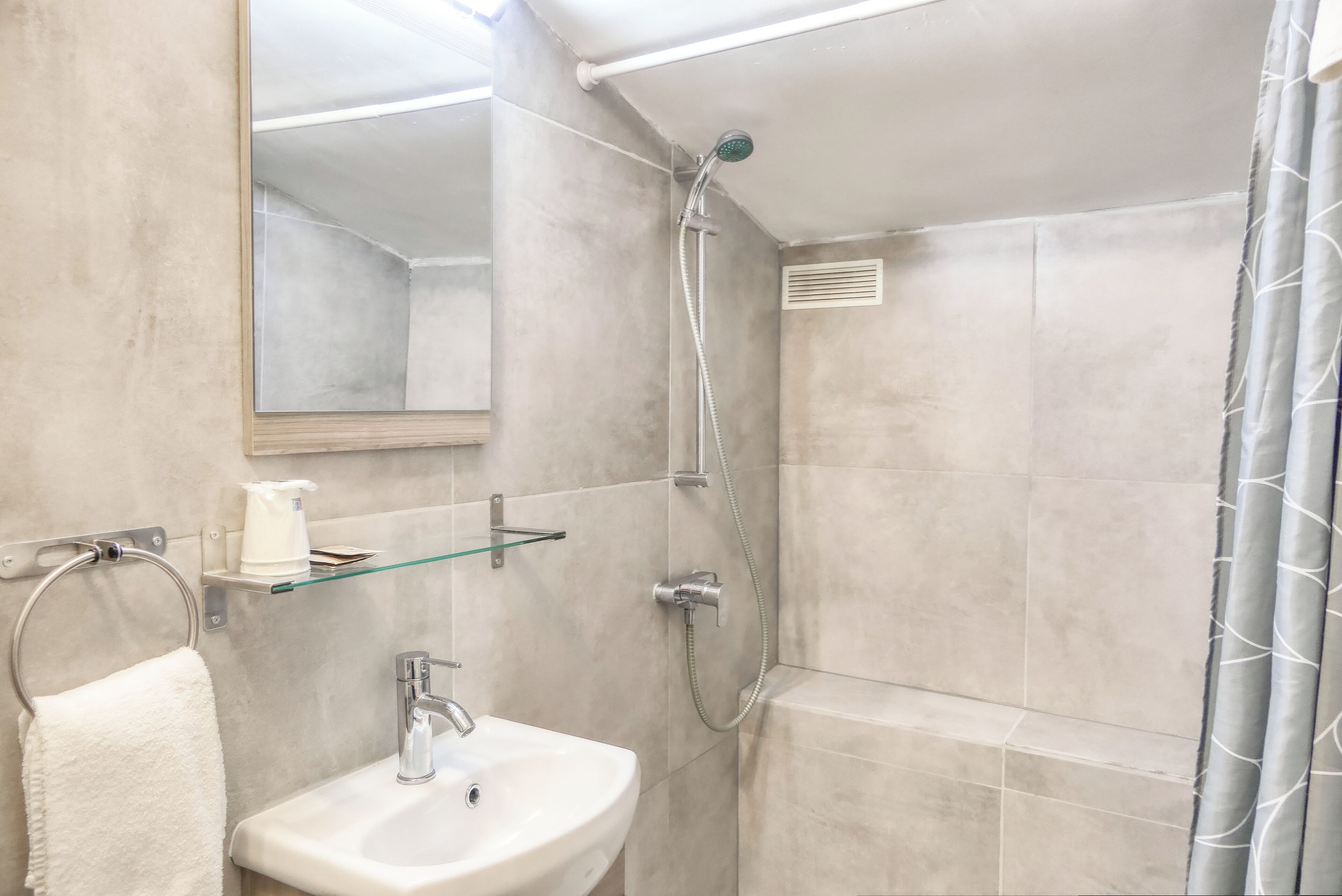 Un baño con lavamanos, espejo, toallero, ducha y repisa de vidrio.