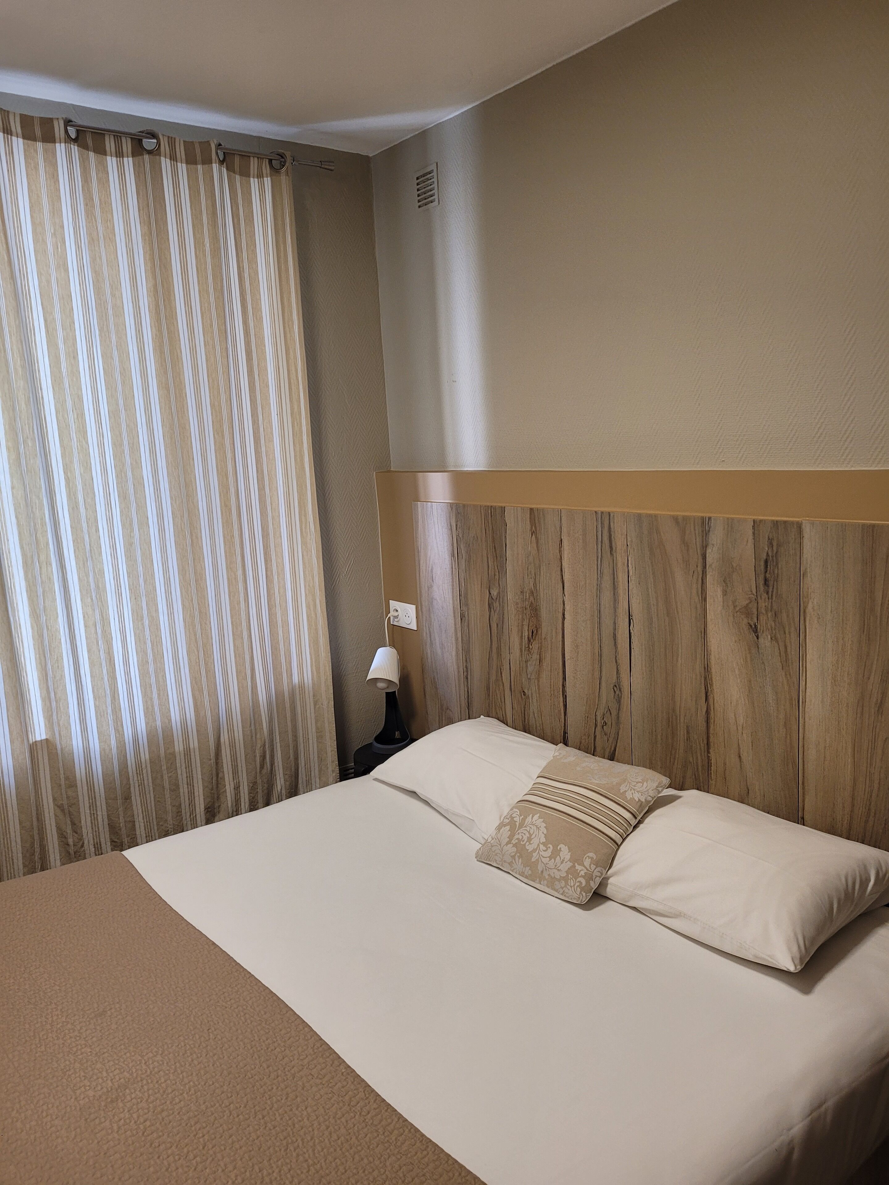 A hotel room with a bed, a nightstand, a lamp, and a window with curtains.