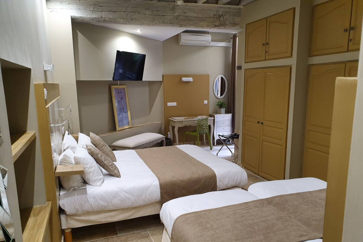 A hotel room with two beds, a desk with a chair, a mirror, and a wardrobe.