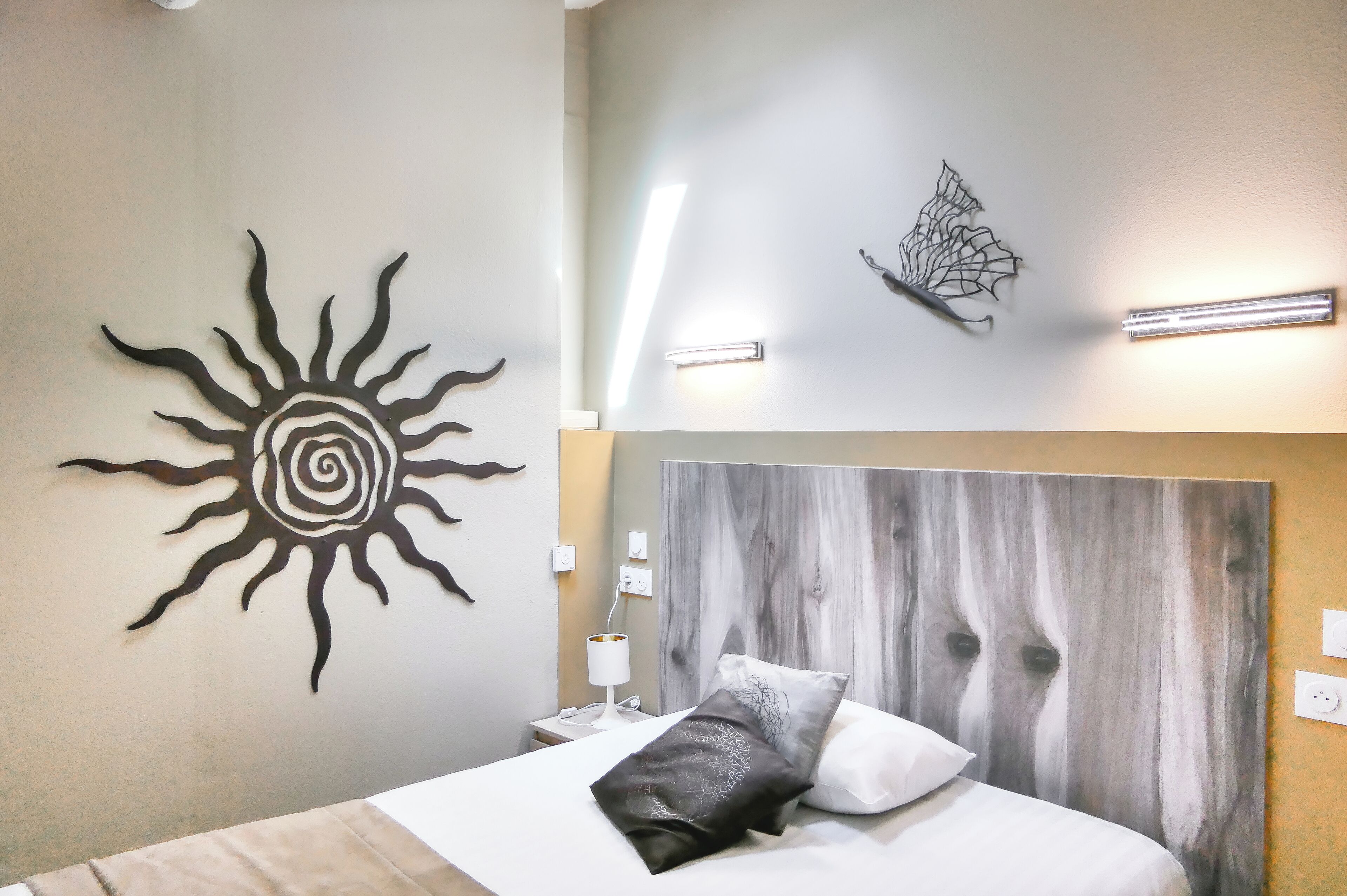 A bedroom with a bed, a headboard, a wall art of a sun, and a wall art of a leaf.