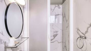 A bathroom with a marble wall, a round mirror, a glass shelf with toiletries, and a towel ring.