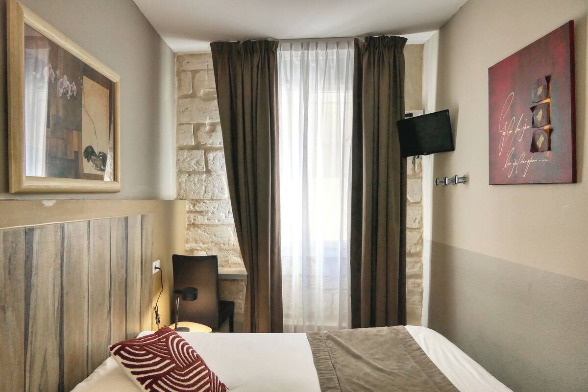 A hotel room with a bed, a desk, a chair, a TV, and a window with curtains.