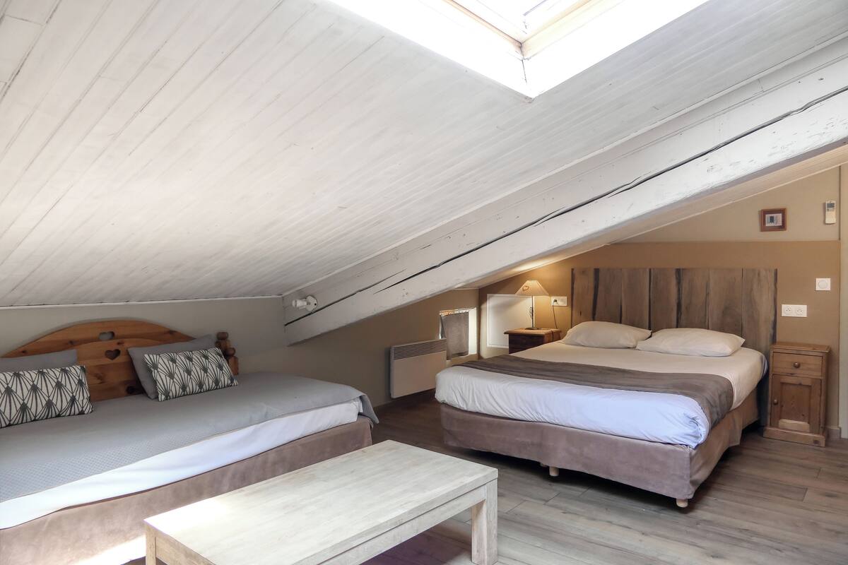 An attic bedroom with two beds, a wooden table, and a skylight.