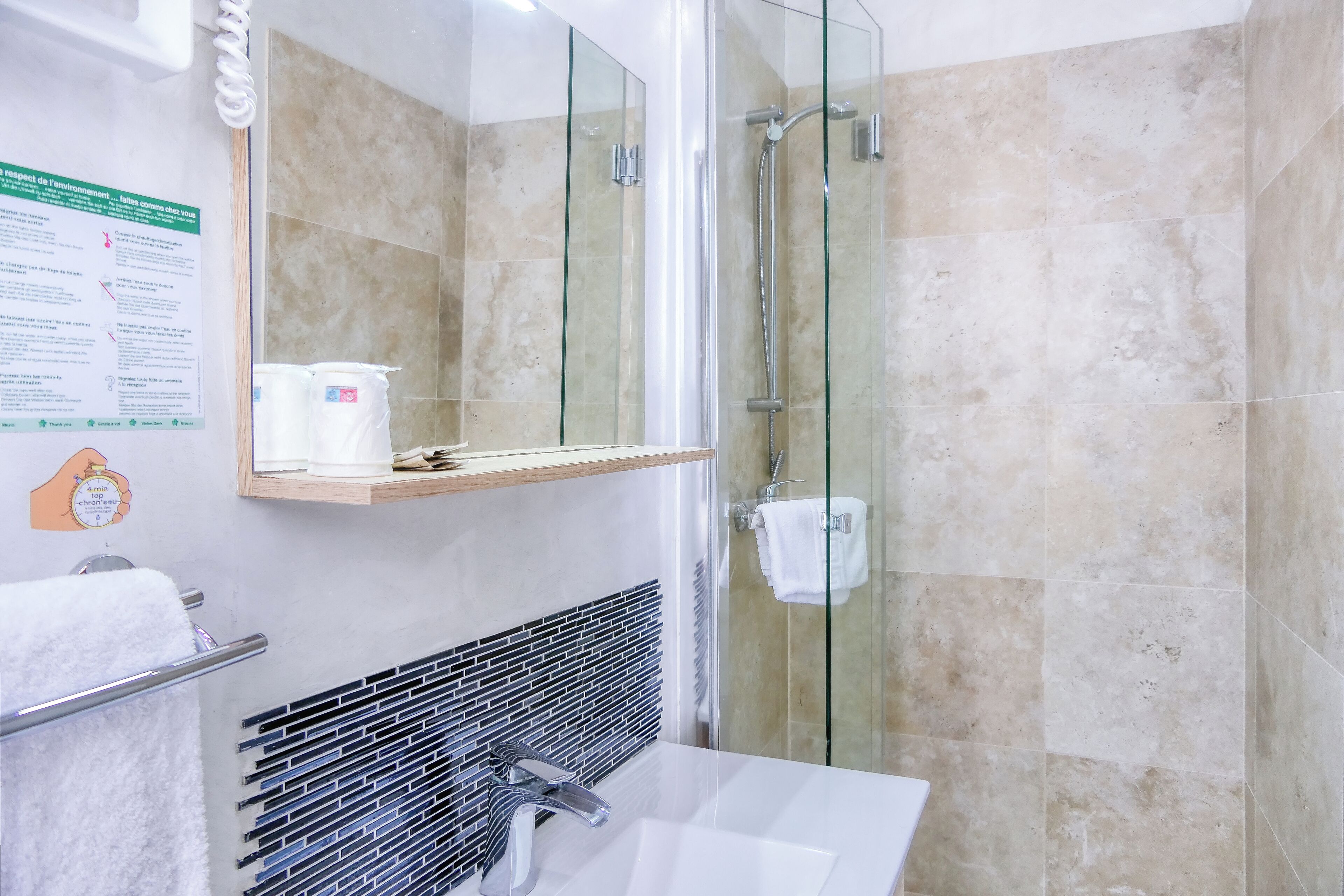 A modern bathroom with a glass shower enclosure, a white sink, and a towel rack.