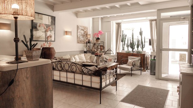 Un grand espace de vie comprenant un lit, une table basse et une lampe. Il y a une fenêtre avec des rideaux, une porte et une plante sur l’appui de fenêtre.