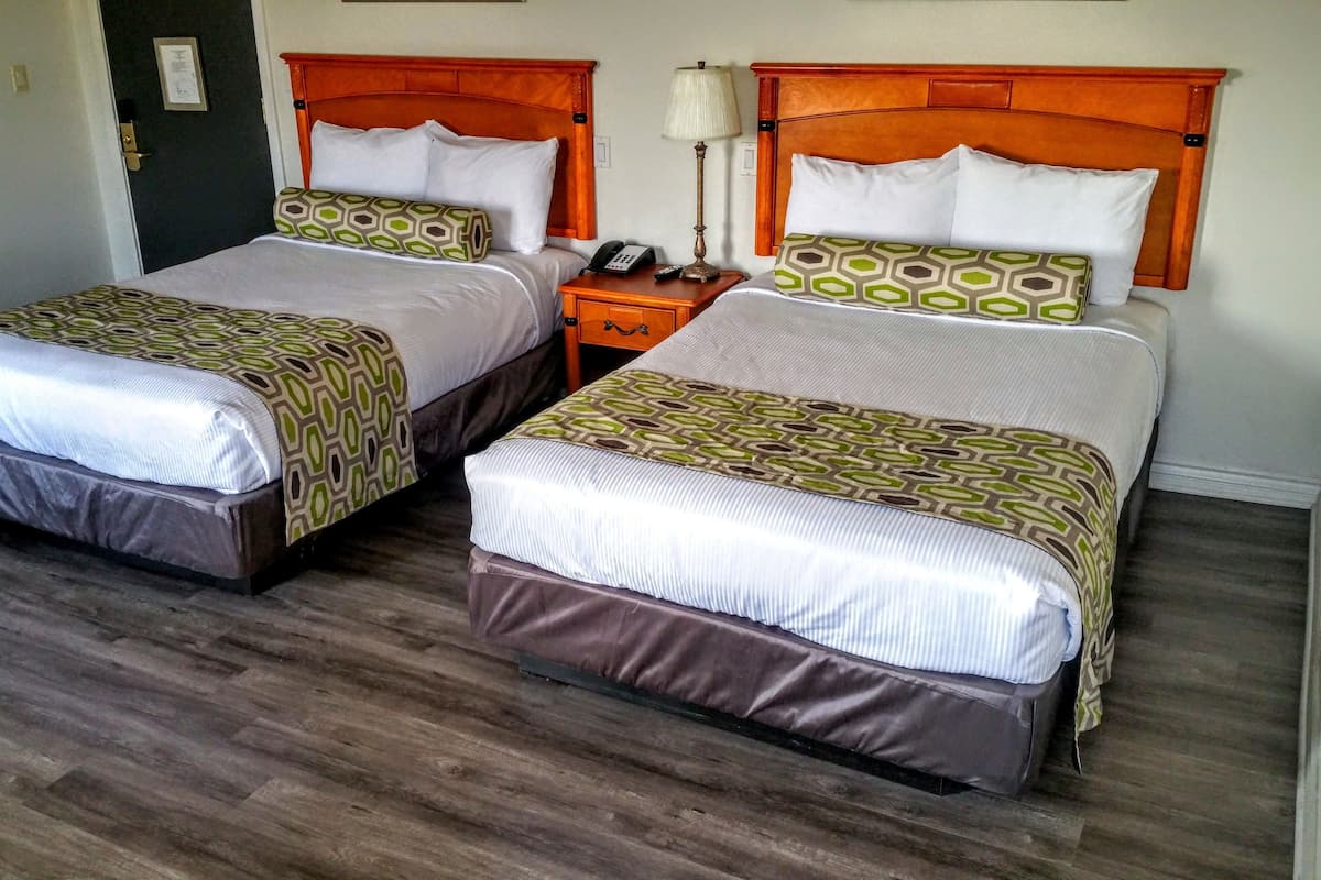 A hotel room with two single beds, wooden headboards, a bedside table with a lamp, and a telephone.