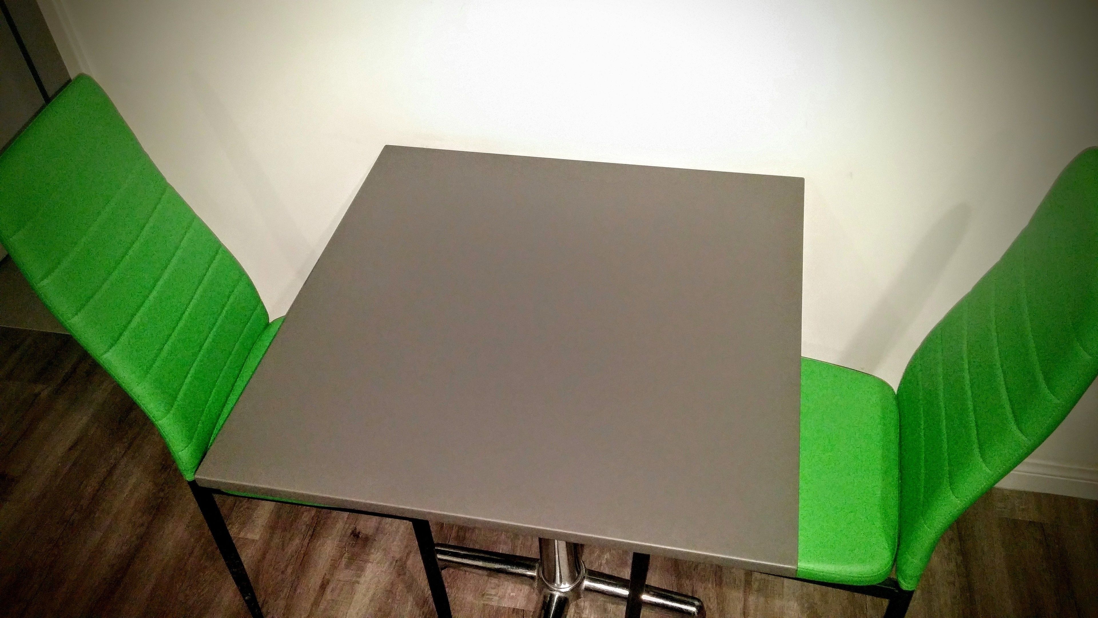 Una mesa pequeña y cuadrada con estructura metálica y una silla verde acolchada a cada lado.