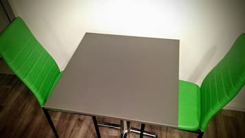 Una mesa pequeña y cuadrada con estructura metálica y una silla verde acolchada a cada lado.