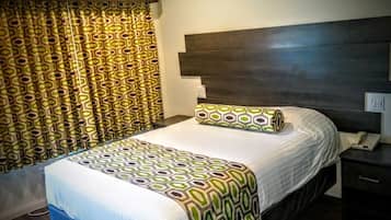 Une chambre d’hôtel comprenant un lit, une table de chevet, un téléphone et un rideau orné d’un motif géométrique.