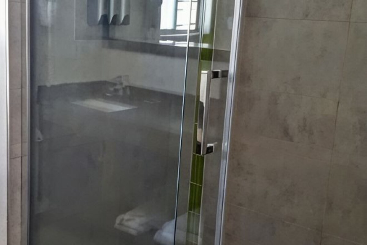 A bathroom with a glass shower enclosure, a visible sink, and a mirror.