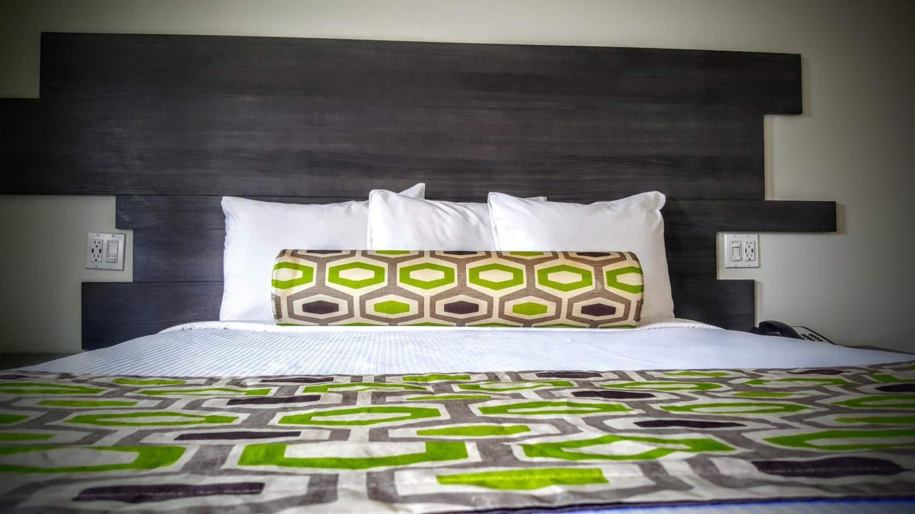 A bed with a patterned bedspread, a headboard with a geometric design, and two bedside lamps.
