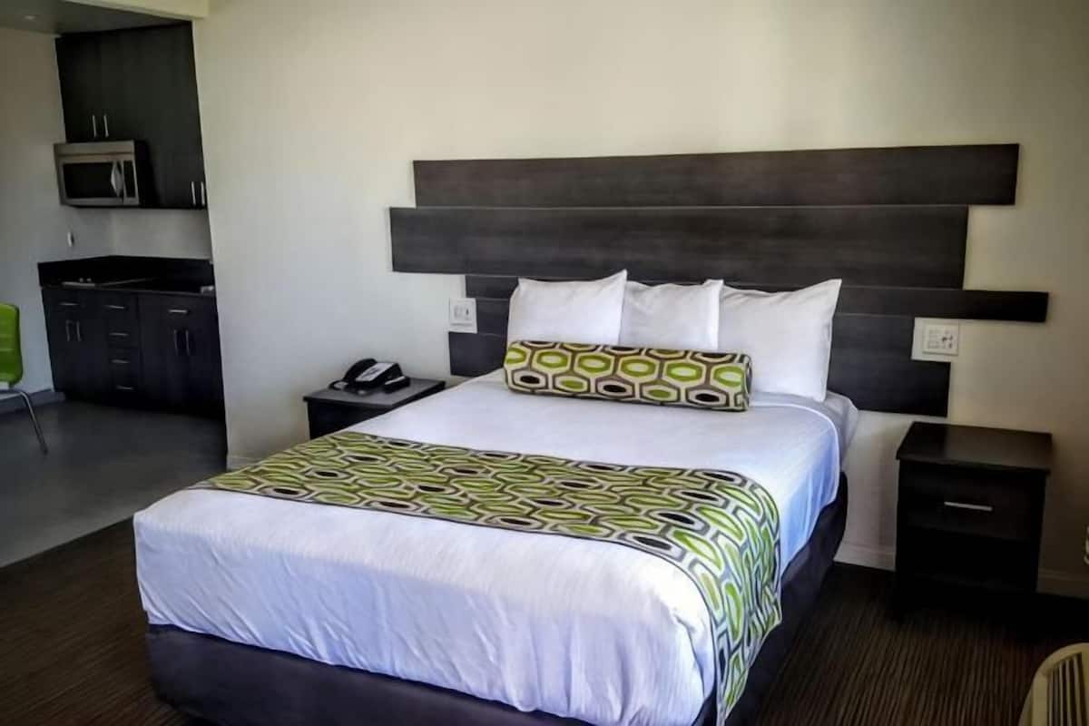 A hotel room with a large bed, a nightstand with a phone, a small table, and a microwave in the kitchen area.