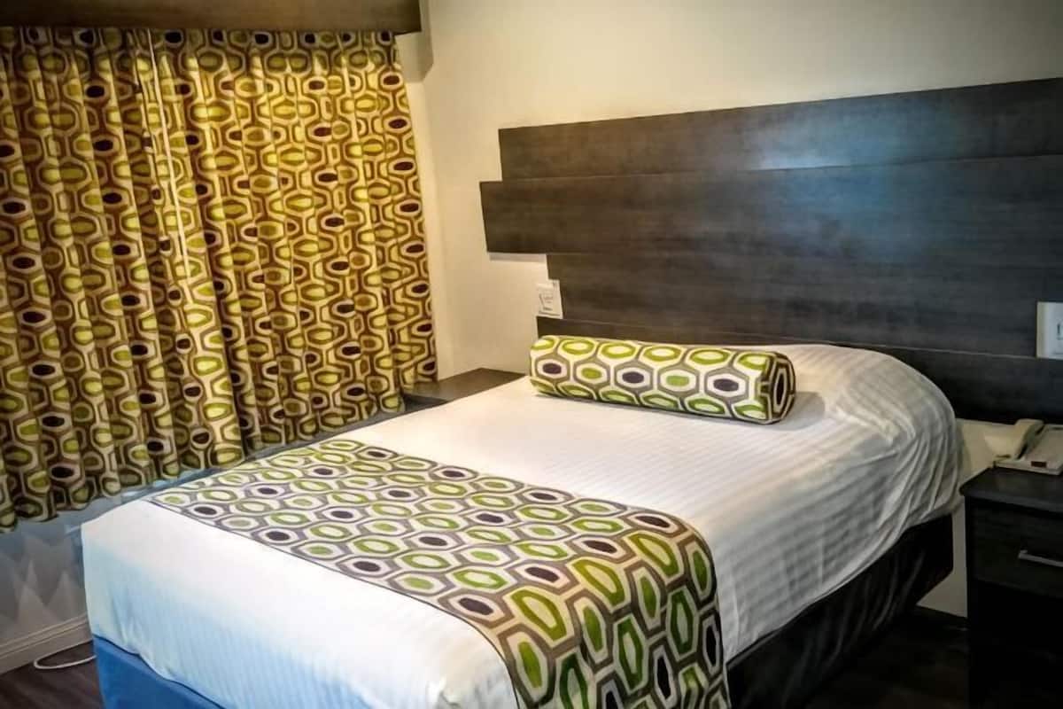 A hotel room with a bed, curtains, a headboard, and a bedside table.