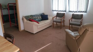 A living room with a sofa, two armchairs, a wooden table, and a bunk bed in the background. - All Seasons Campground & Cabins (Ninilchik)