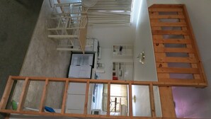 A room with a kitchen area, a wooden ladder, and a window with blinds. - All Seasons Campground & Cabins (Ninilchik)