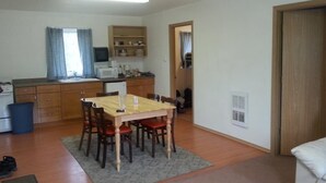 A compact living space with a dining area, kitchenette, and a door leading to another room. - All Seasons Campground & Cabins (Ninilchik)